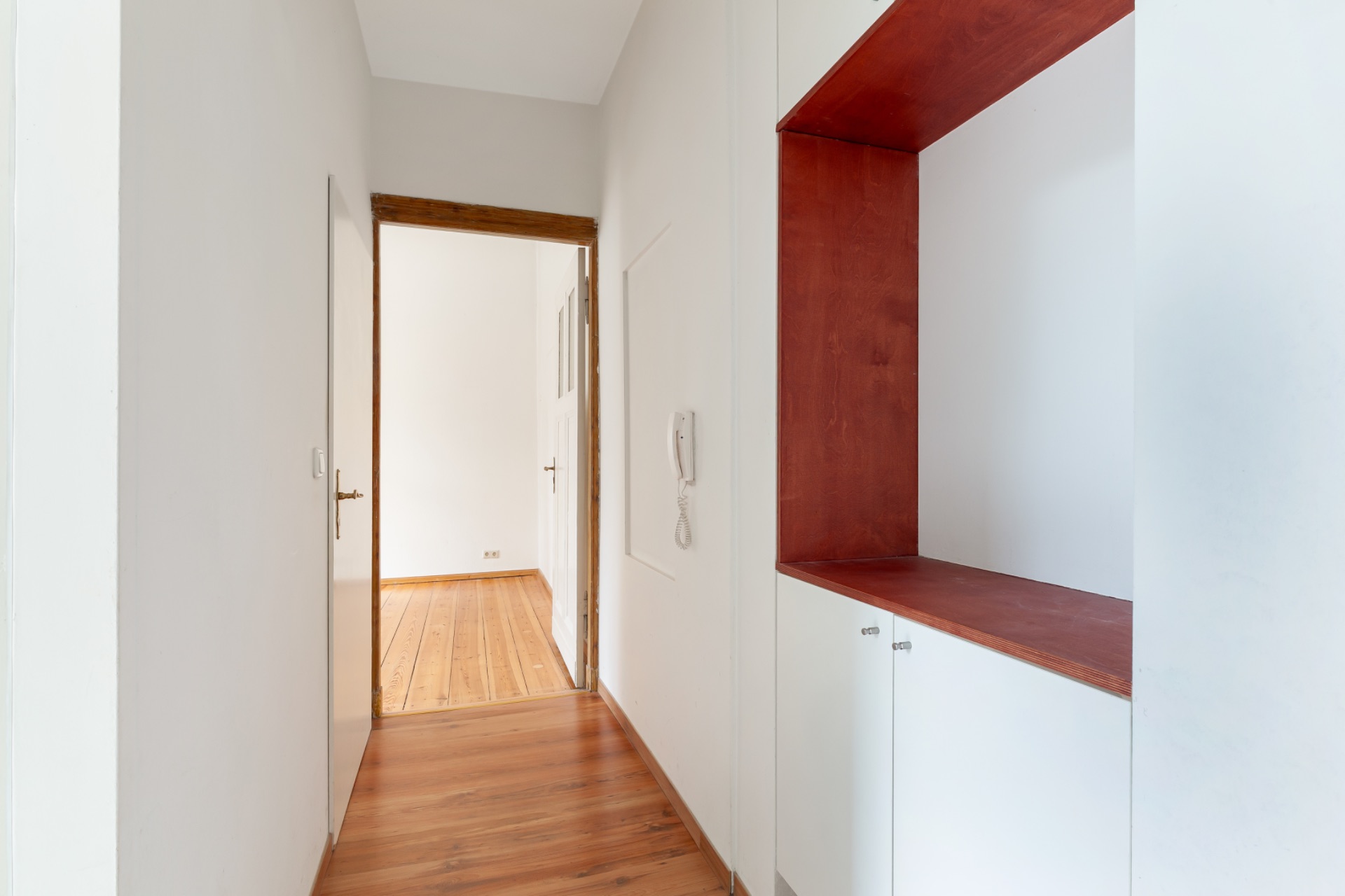 Heller Flur mit Holzfußboden, weißen Wänden und einem Einbauschrank mit roter Nische.