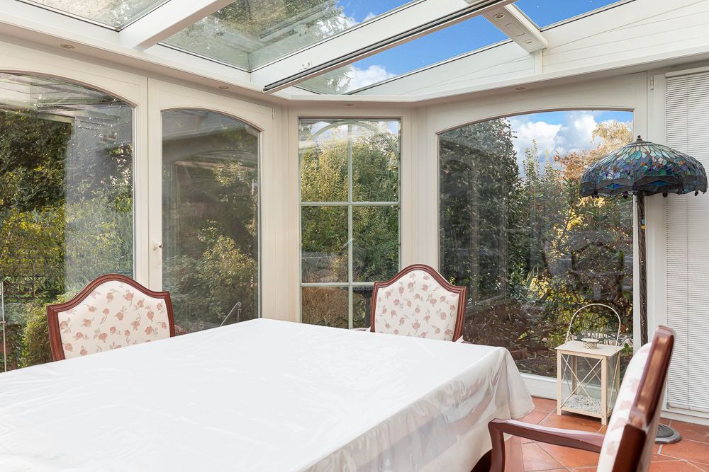 Wintergarten mit Glastüren, Esstisch mit weißer Decke und vier gepolsterten Stühlen.