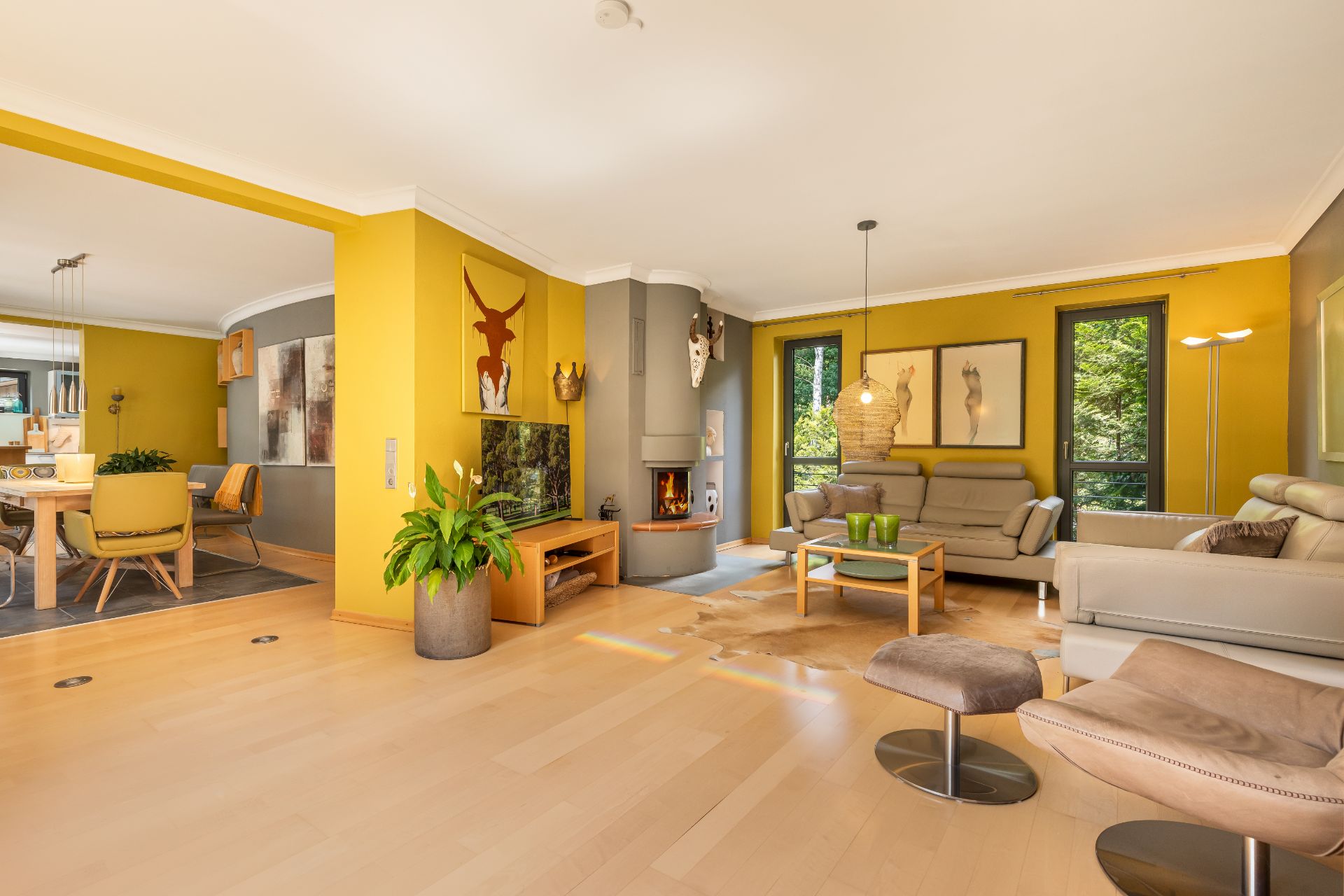 Modernes Wohnzimmer mit gelben Wänden, Kamin, Sofas und Esstisch, viel Tageslicht.