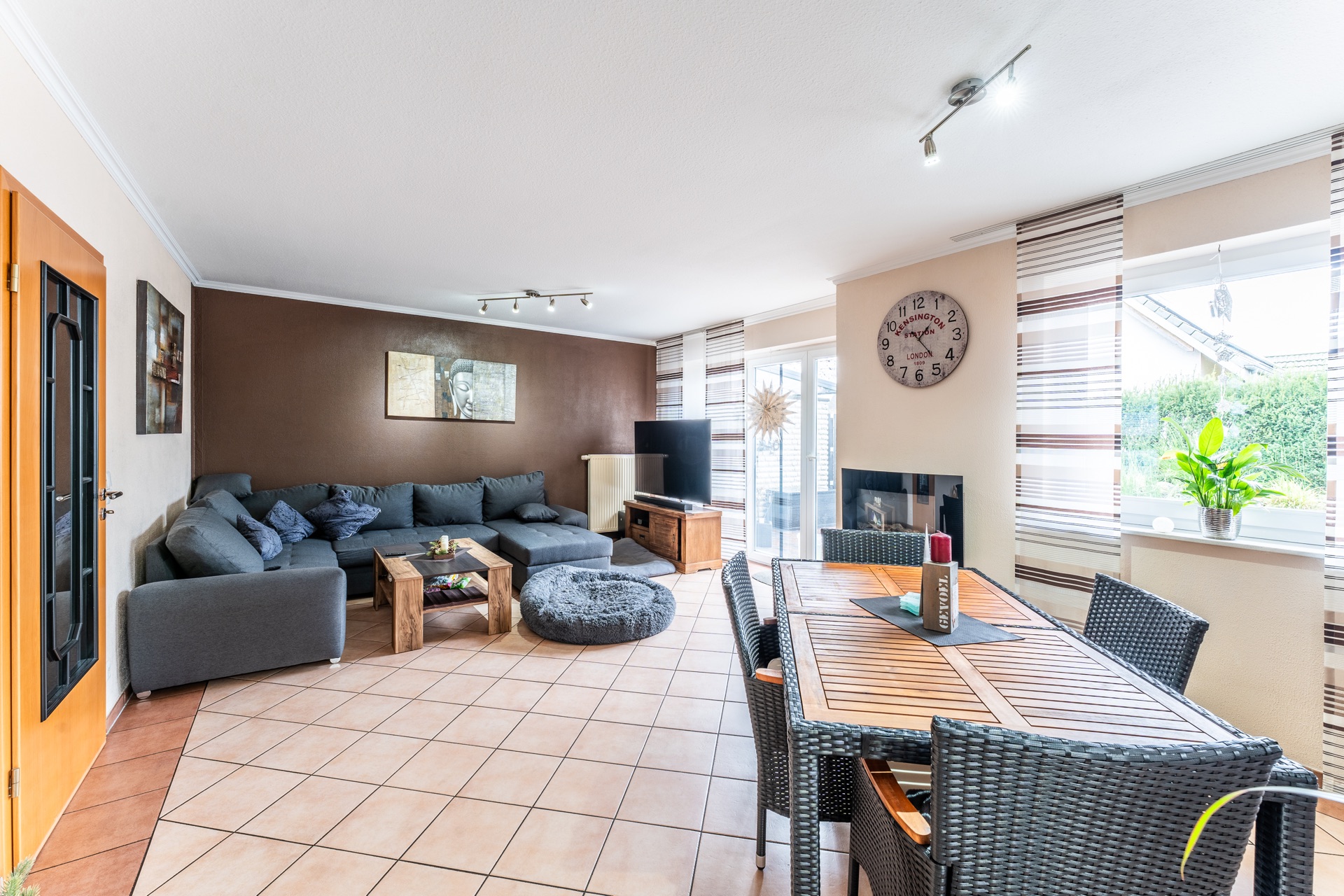 Helles Wohnzimmer mit großer Eckcouch, Esstisch, Fernseher und vielen Fenstern.