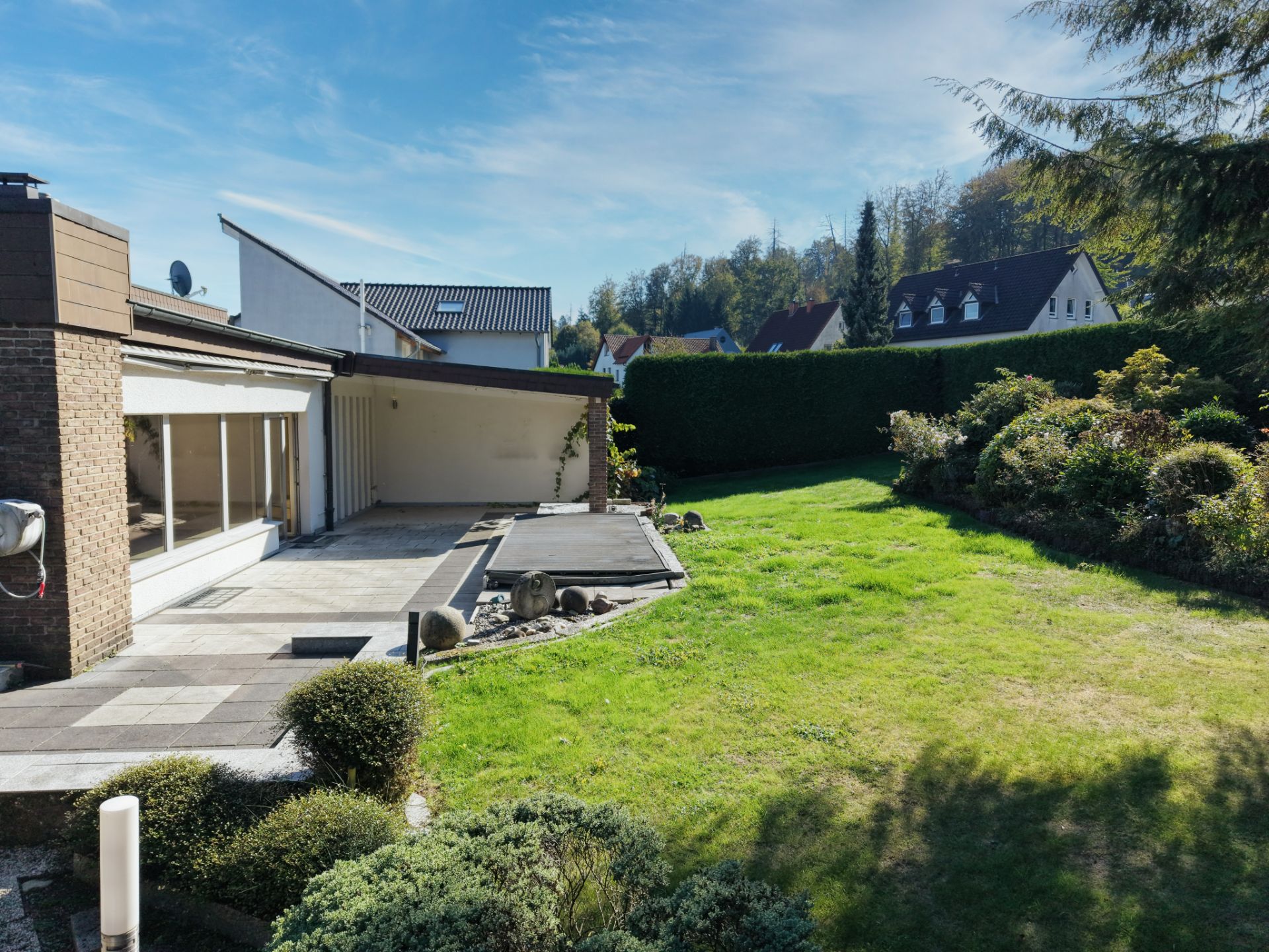 Garten mit Terrasse und kleinem Steingarten hinter einem Wohnhaus bei sonnigem Wetter.