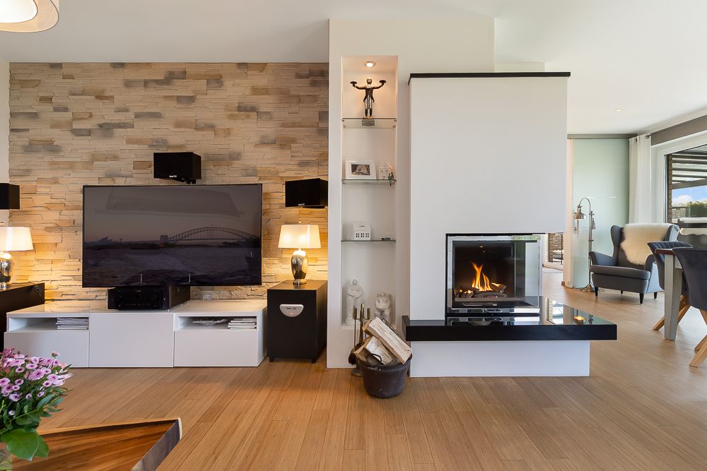 Modernes Wohnzimmer mit Kamin, Fernseher, Holzfußboden und heller Steinwand.