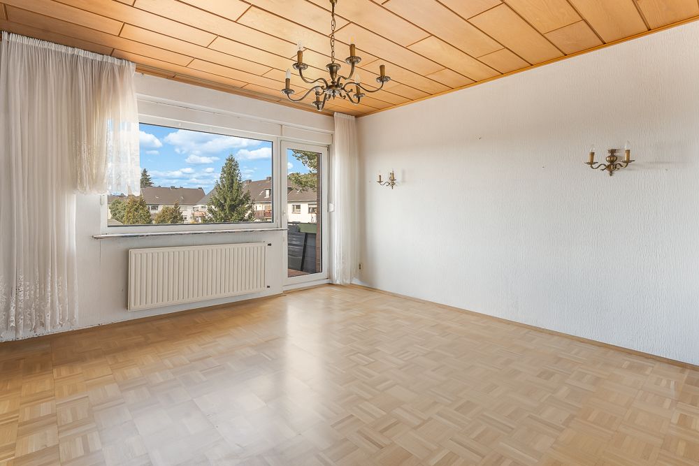 Leeres Wohnzimmer mit Parkettboden, großem Fenster, Vorhängen und Deckenleuchte.