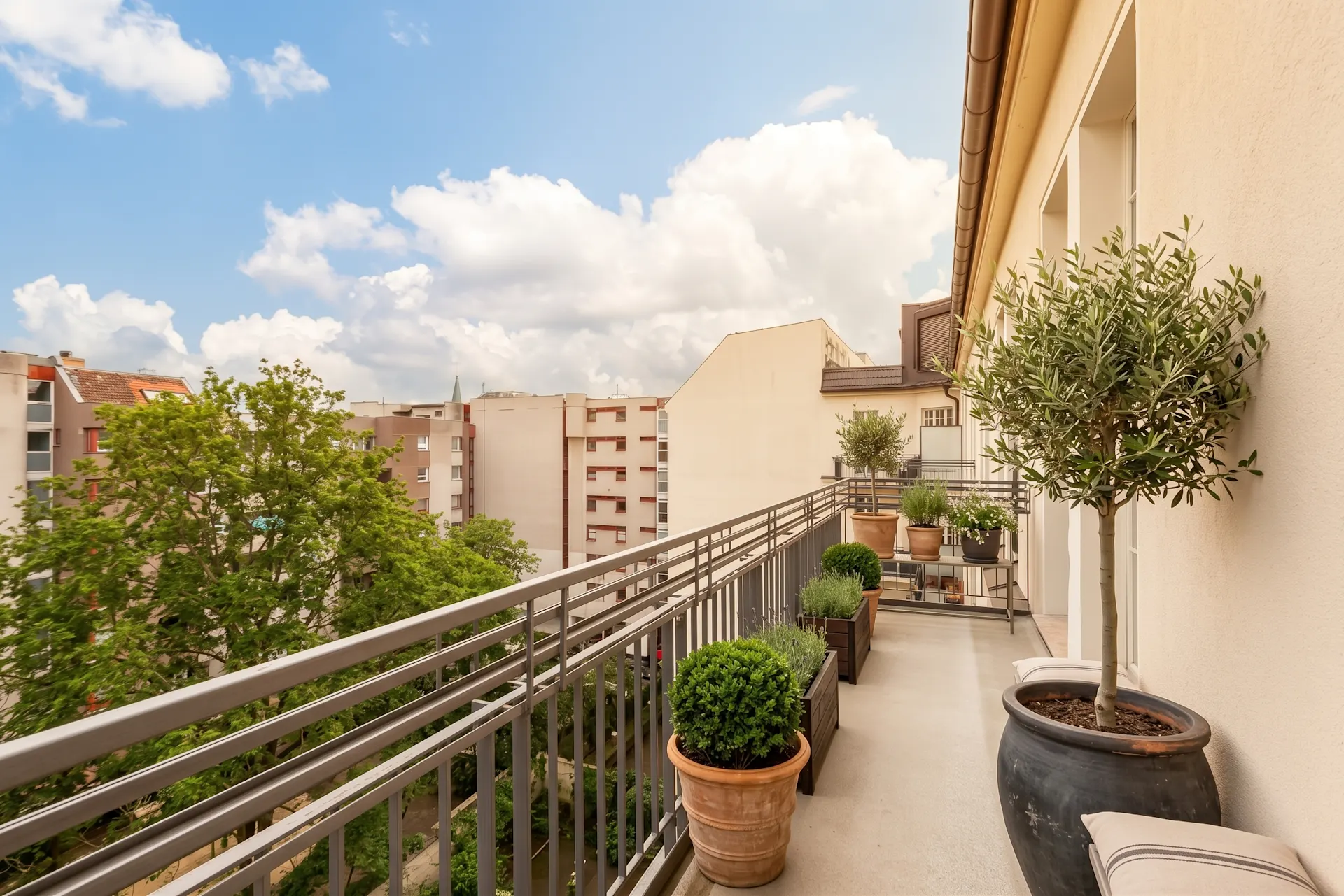 Balkon mit Pflanzen in Töpfen, Blick auf Bäume und benachbarte Wohngebäude.