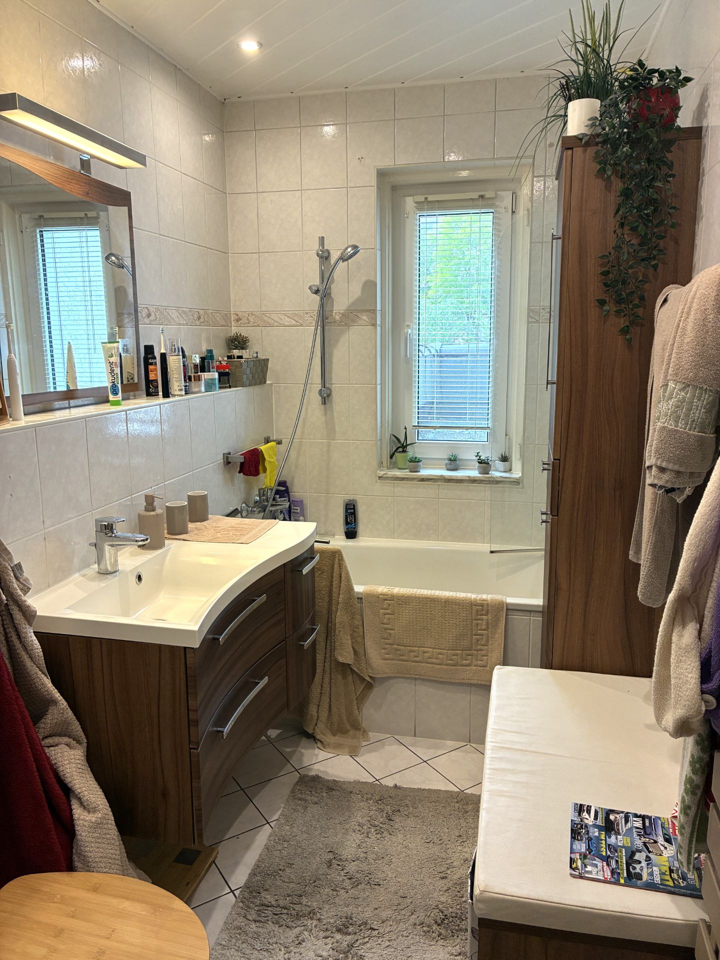 Modernes Badezimmer mit Waschbecken, Badewanne, Holzschränken, Bank und Fenster.