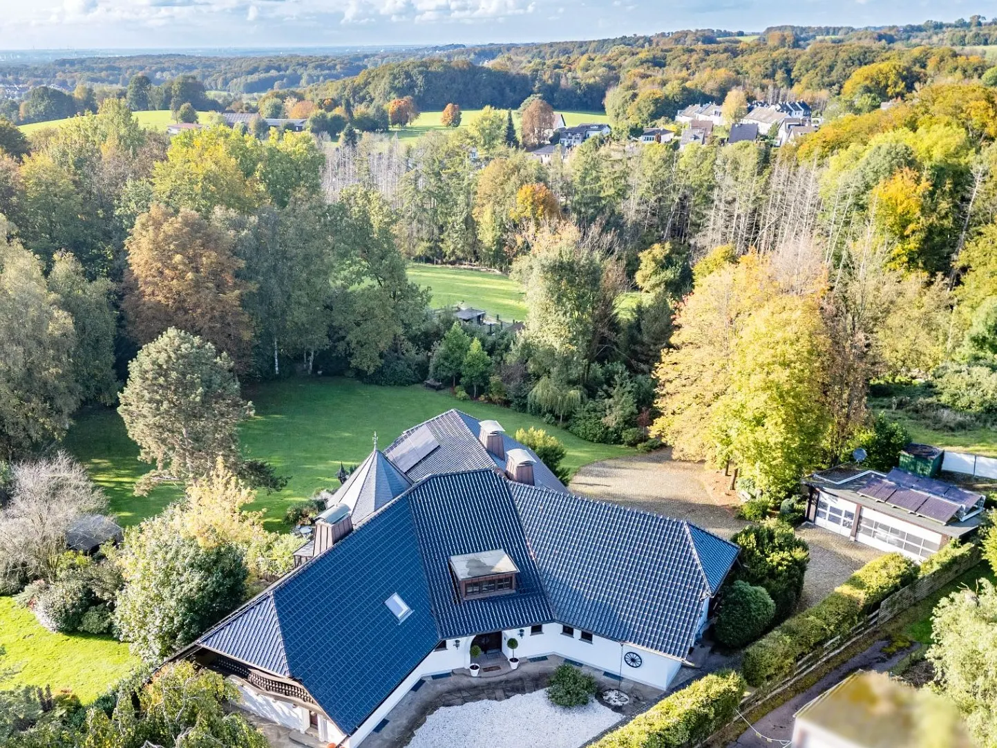 Luftaufnahme eines Hauses mit dunklem Dach und großem Garten, umgeben von Bäumen.