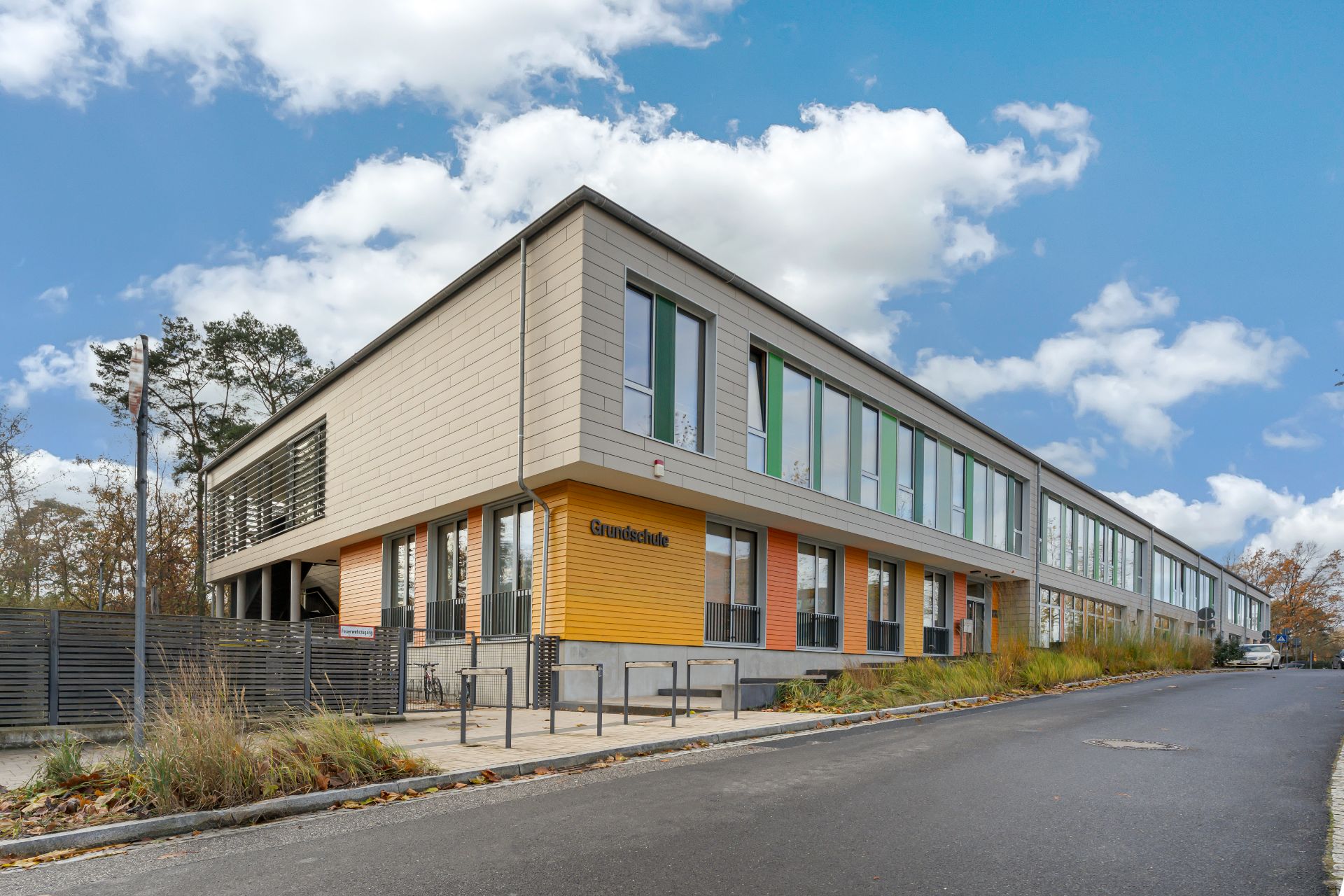 Modernes, zweistöckiges Schulgebäude mit großen Fenstern und gelber Fassade.