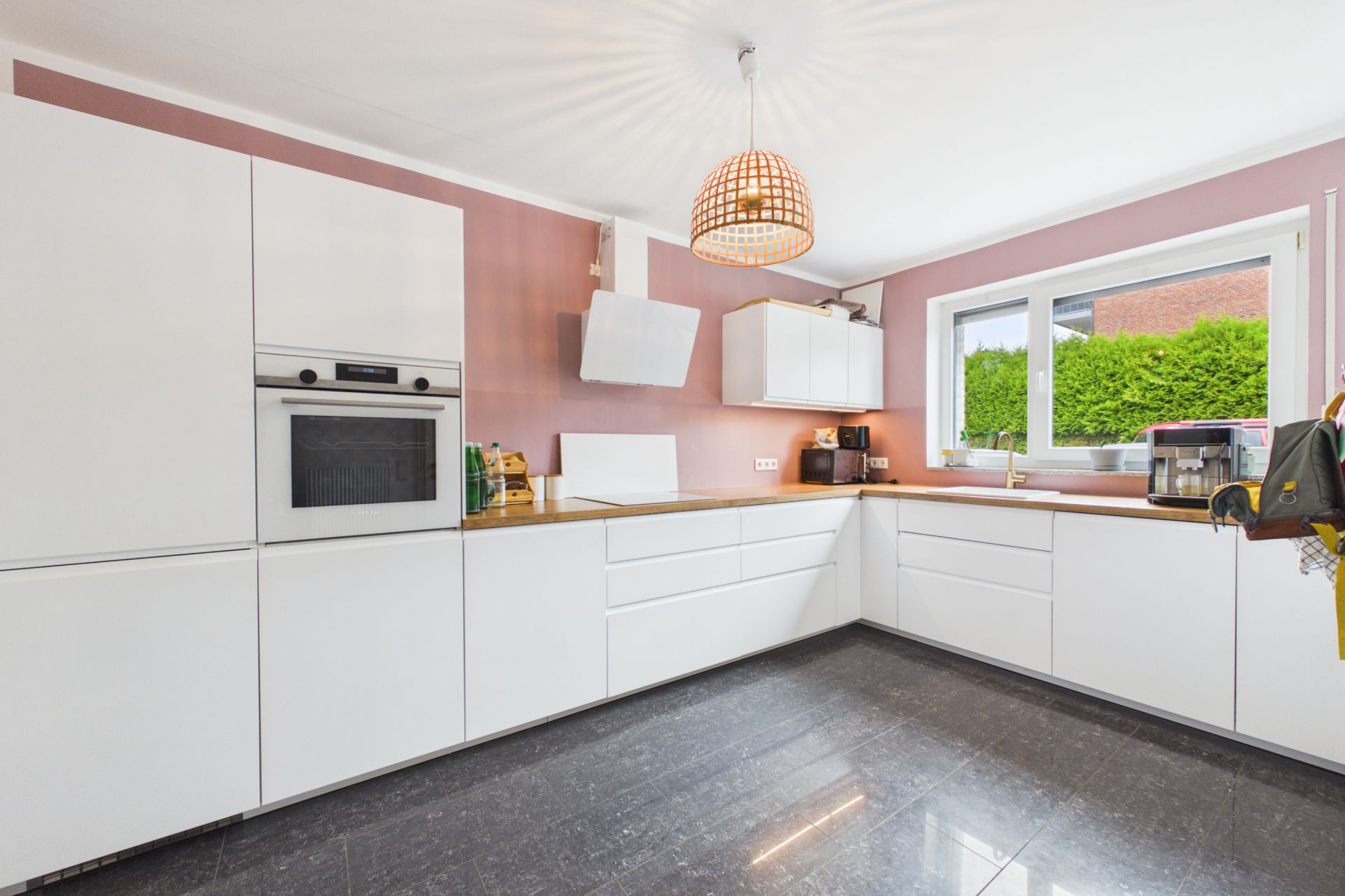 Moderne Küche mit weißen Schränken, Holzarbeitsplatte und großem Fenster.