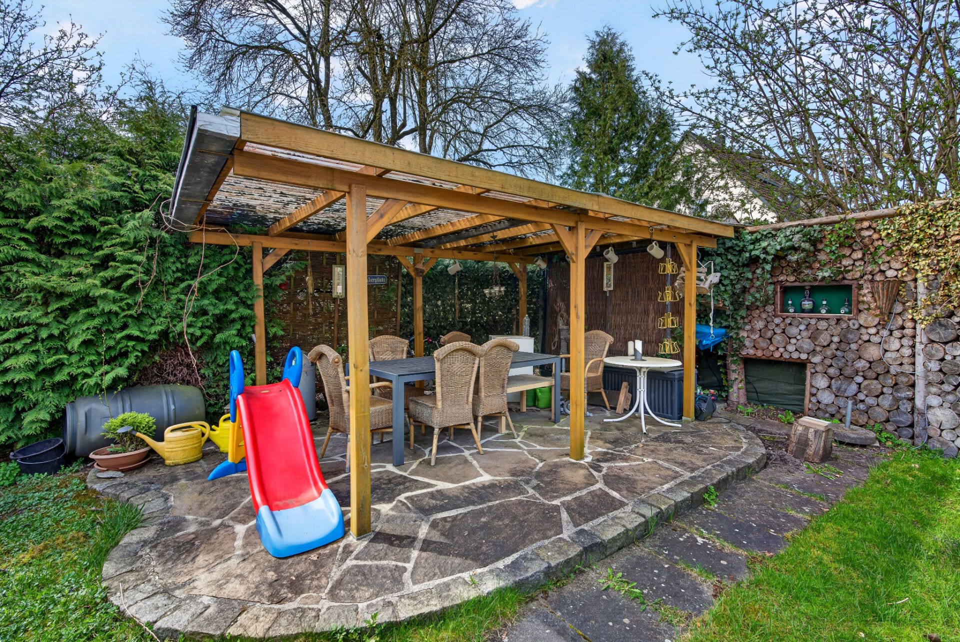 Überdachte Terrasse mit Esstisch, Stühlen und Kinderrutsche im Garten.