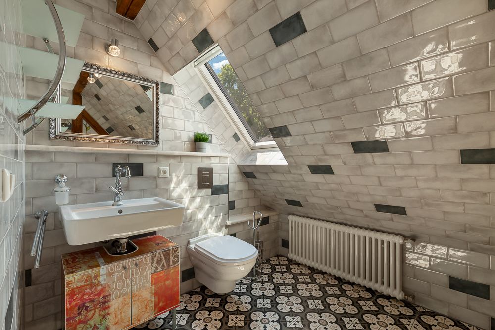 Kleines Badezimmer mit Waschbecken, WC, Spiegel, Radiator und Dachfenster unter einer Schräge.