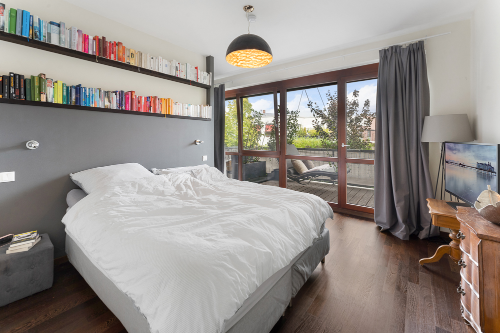 Helles Schlafzimmer mit Doppelbett, Bücherregalen, Balkonzugang und großen Fenstern.