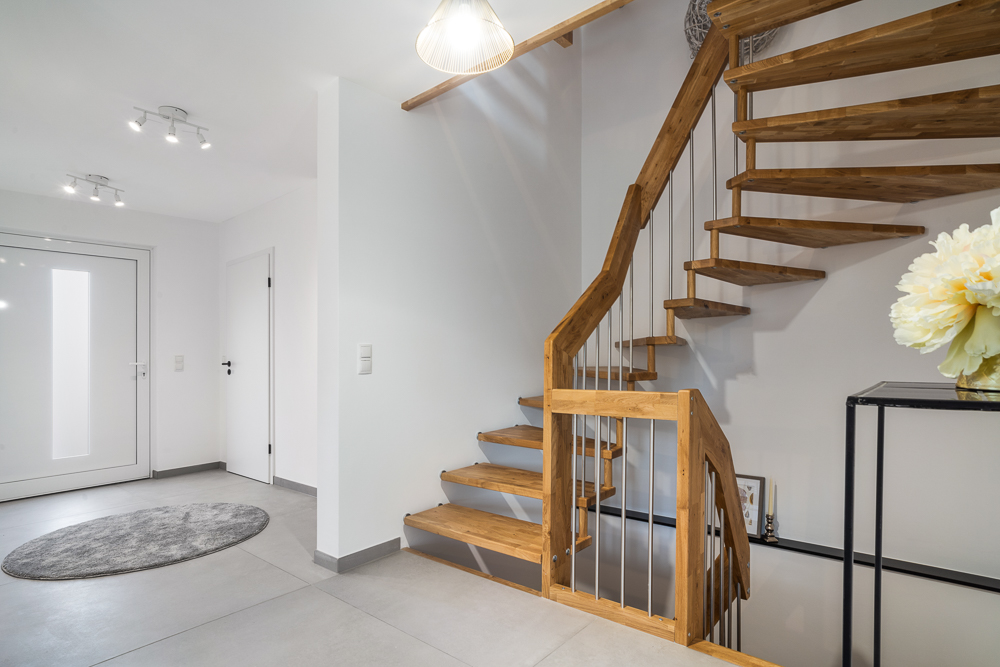 Moderner Flur mit Holztreppe, weißer Tür, rundem Teppich und Tisch mit Blumen.
