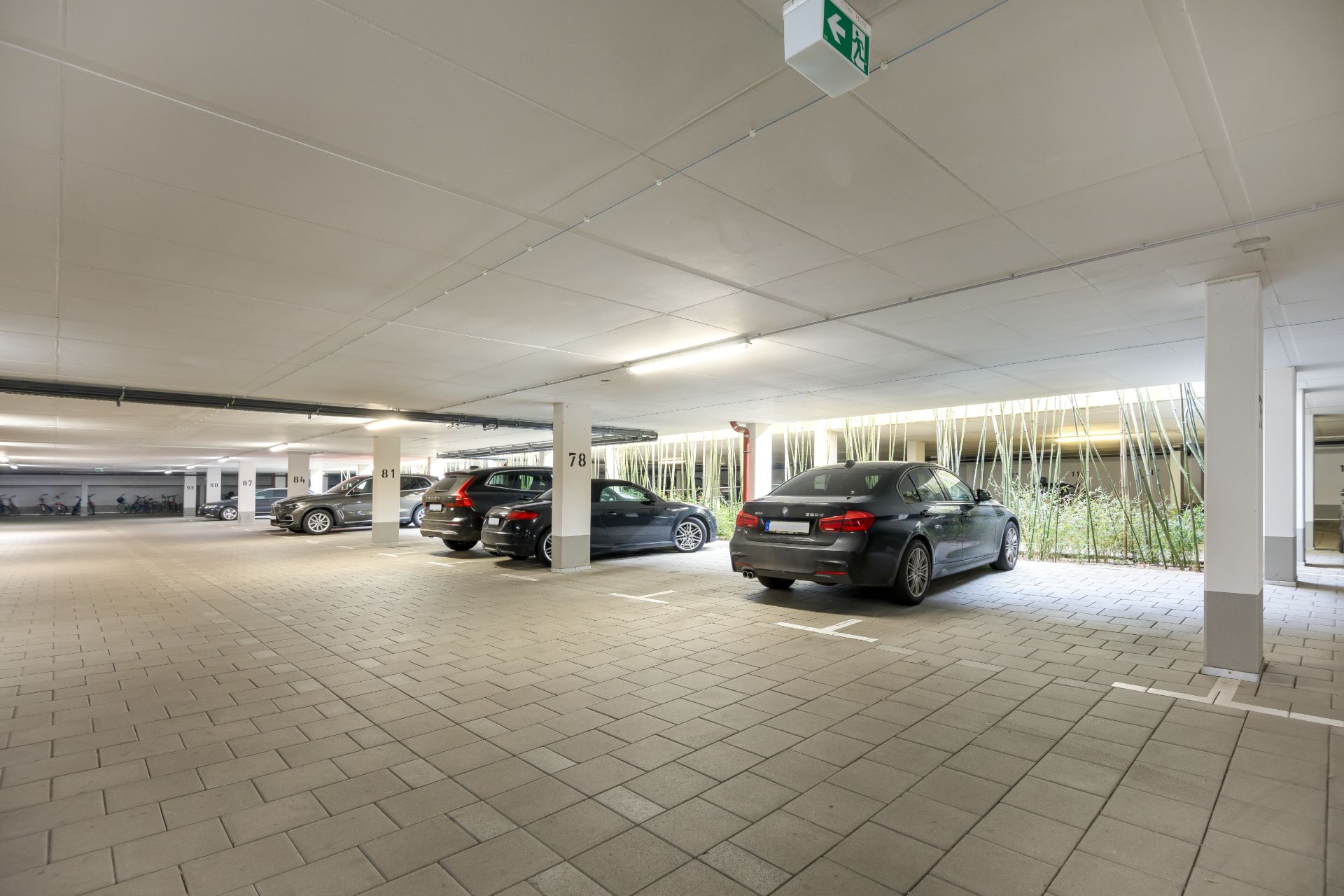 Helle Tiefgarage mit mehreren geparkten Autos und nummerierten Stellplätzen.