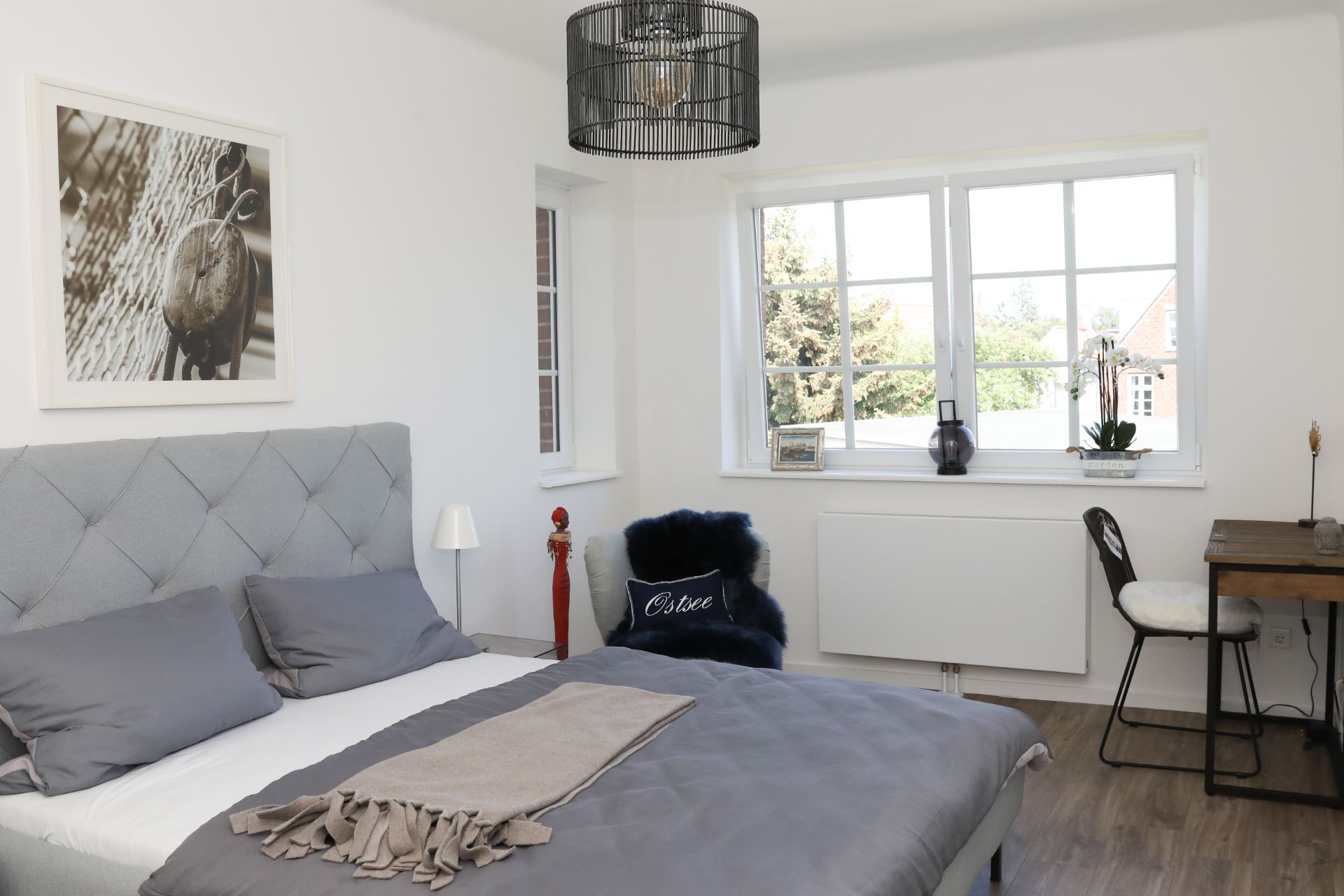 Helles Schlafzimmer mit Doppelbett, Schreibtisch und großem Fenster mit Blick nach draußen.