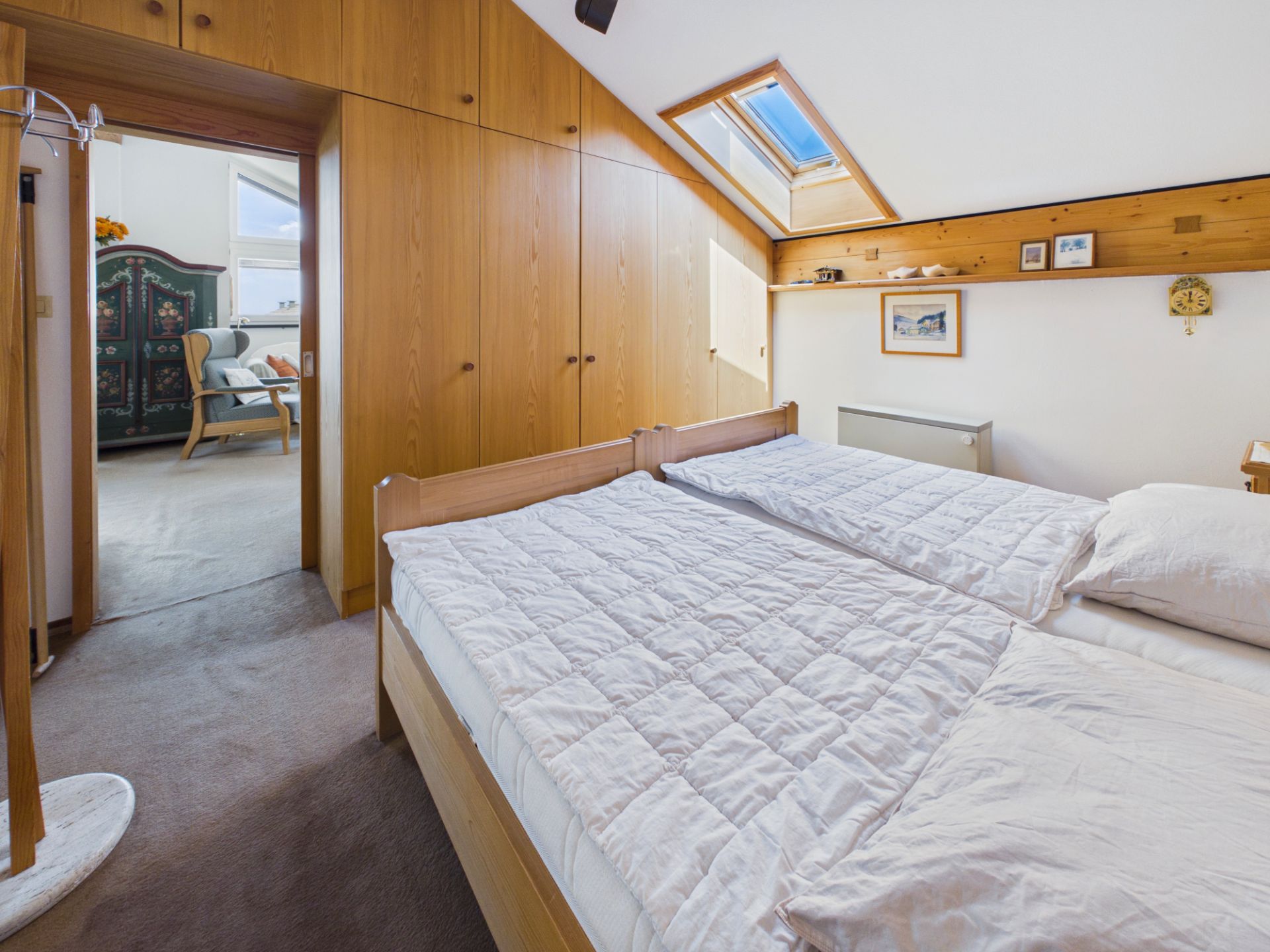 Schlafzimmer mit zwei Einzelbetten, Holzschränken und Dachfenster, Blick ins angrenzende Zimmer.