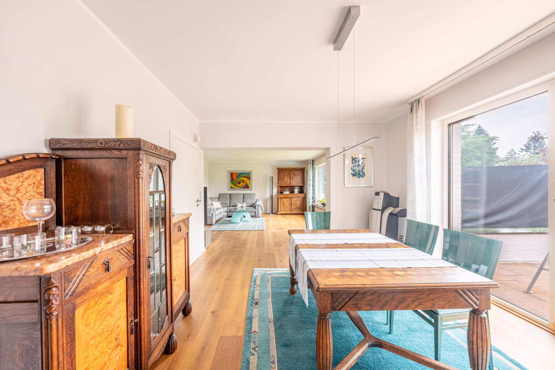 Esszimmer mit Holztisch, Stühlen, Teppich und großen Fenstern, danach ein Wohnzimmer.