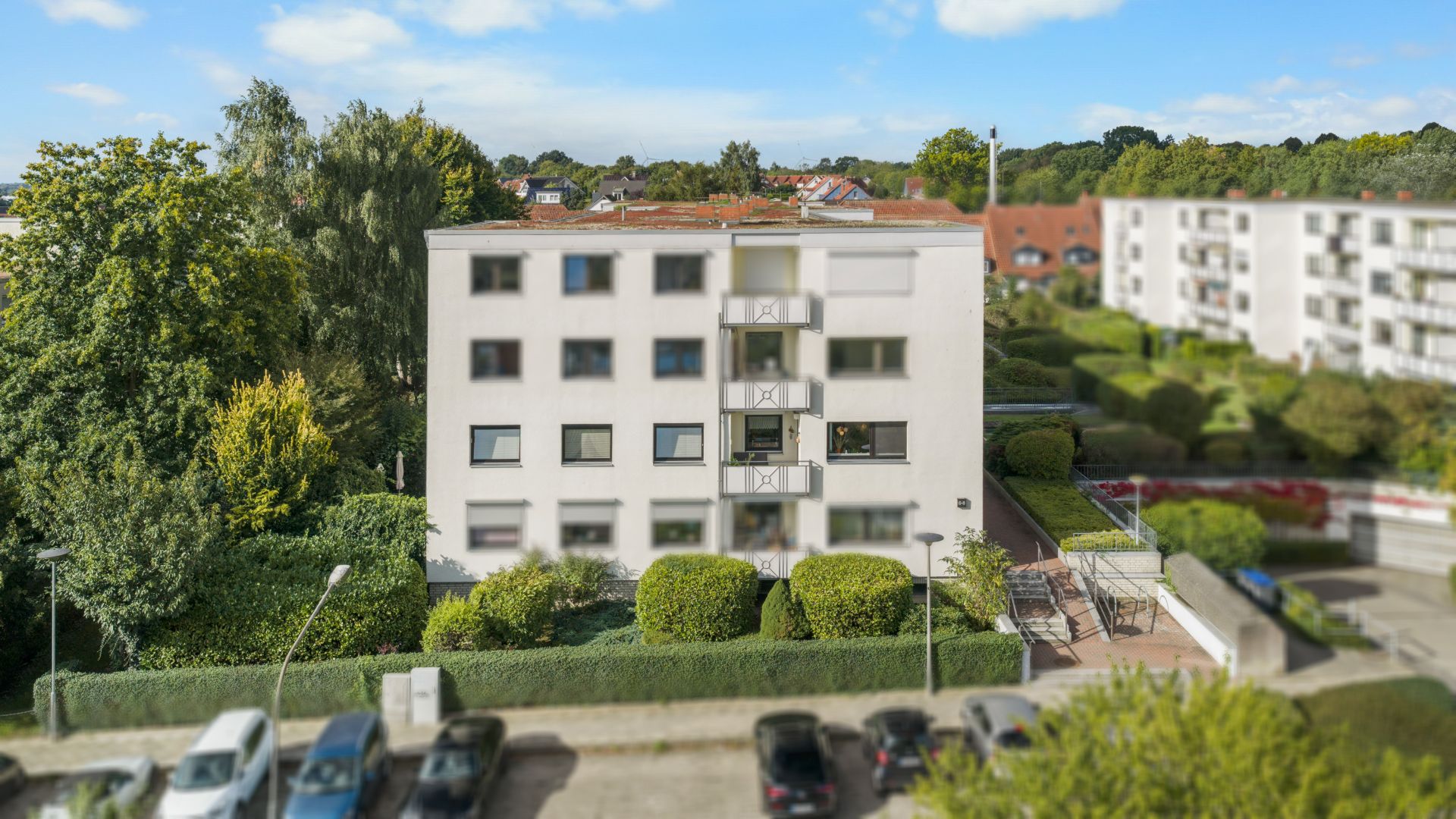 Mehrfamilienhaus mit vier Etagen, umgeben von Bäumen und geparkten Autos davor.