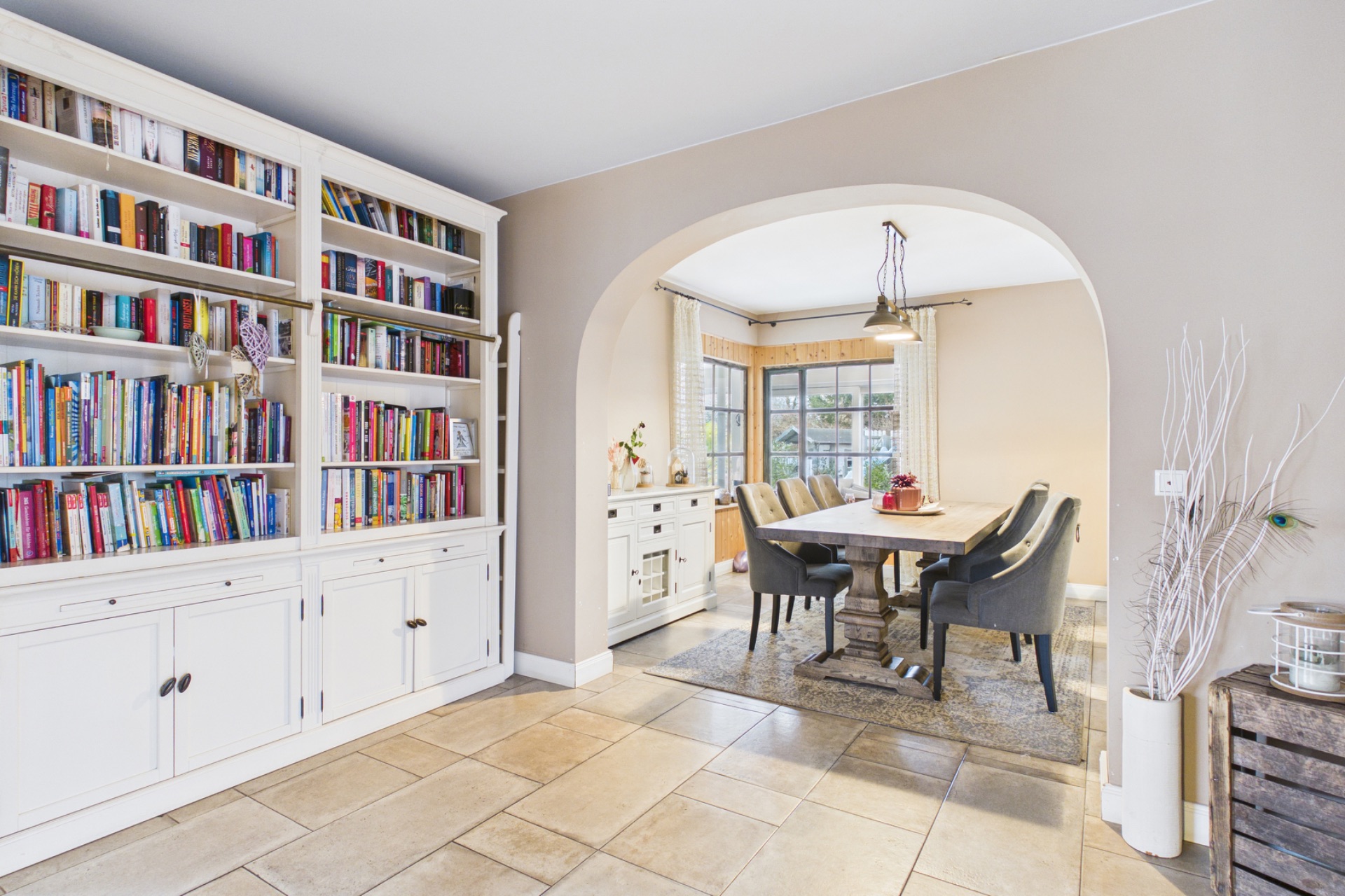 Helles Esszimmer mit großem Fenster, Holztisch, sechs Stühlen und Bücherregal.