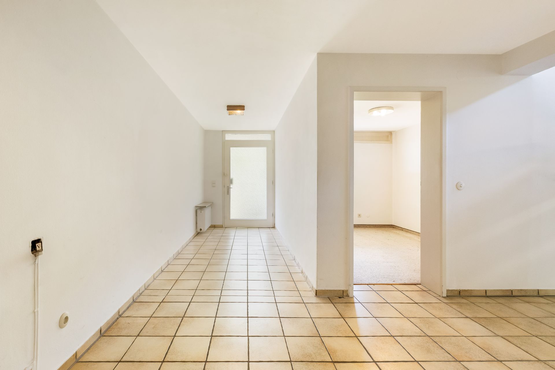 Heller Flur mit Fliesenboden und Zugang zu einem weiteren Zimmer mit Teppichboden.