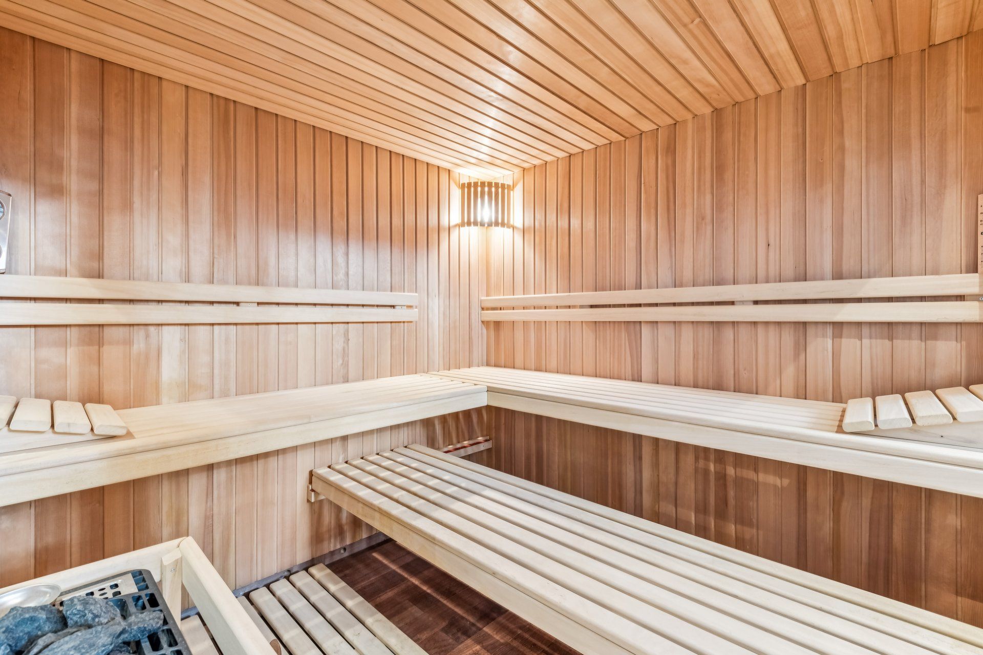 Innenansicht einer Holzsauna mit Bänken und einer Lampe an der Wand.
