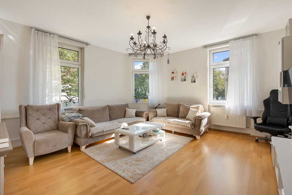 Helles Wohnzimmer mit Sofas, Couchtisch, Teppich und Kronleuchter, drei Fenstern und Vorhängen.