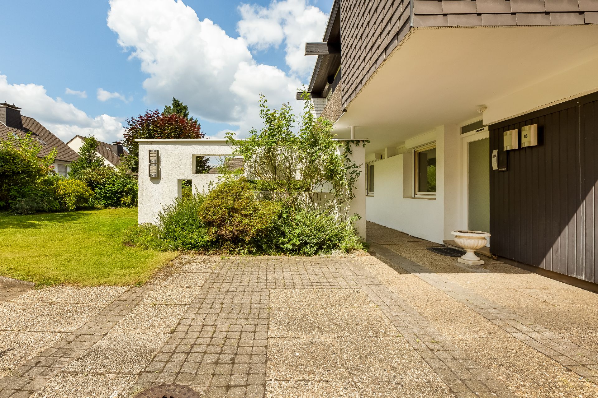 Eingangsbereich eines Wohnhauses mit überdachtem Eingang und Garten im Vordergrund.