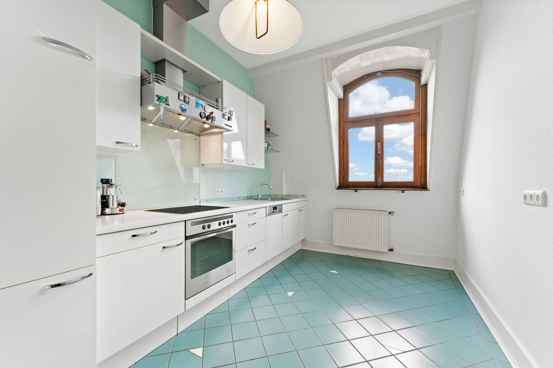 Moderne Einbauküche mit weißen Schränken, Herd und großem Fenster mit Blick nach draußen.