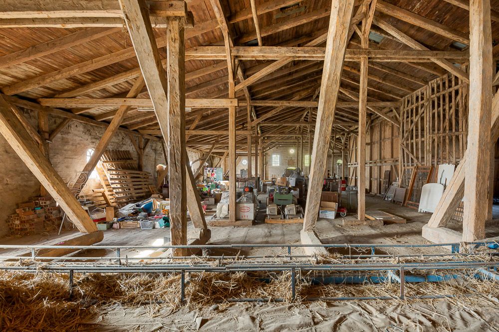 Großer Dachboden mit Holzbalken, Lagergegenständen und etwas Stroh auf dem Boden.