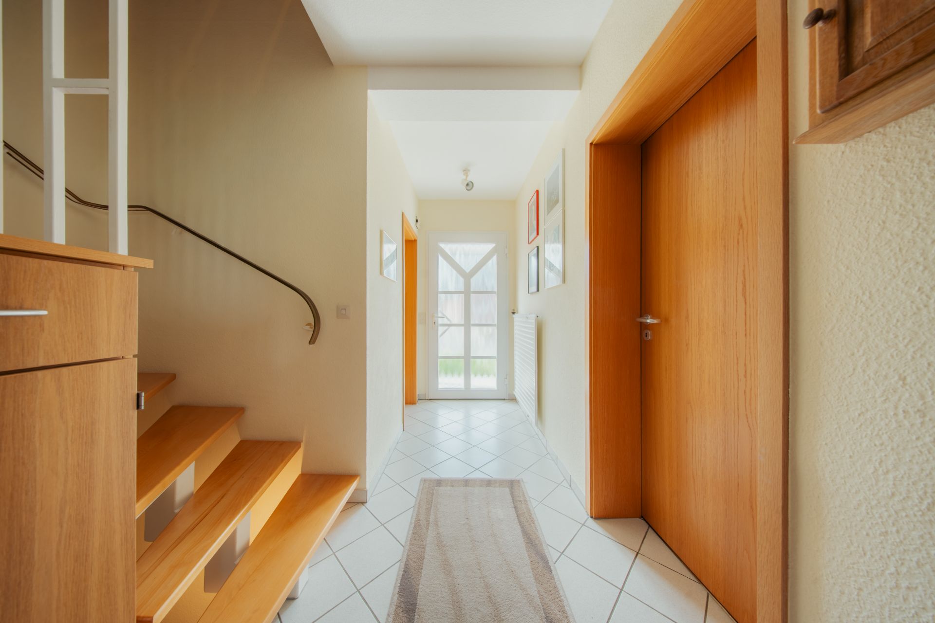 Heller Flur mit Holztreppe, weißen Fliesen und Holztüren.