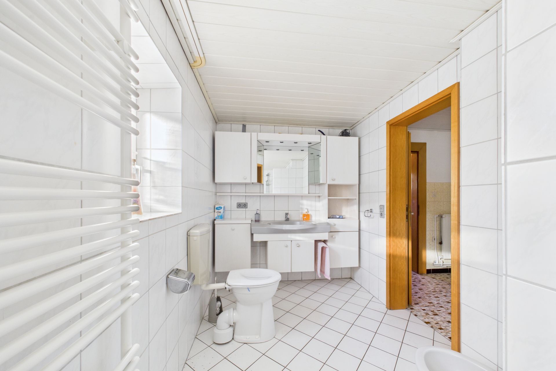 Helles Badezimmer mit Toilette, Waschbecken, Spiegel und weißen Fliesen.