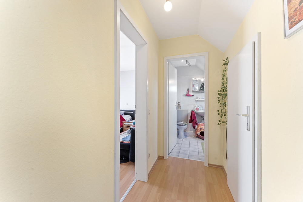 Heller Flur mit Türen zu einem Wohnzimmer und einem Badezimmer, Holzboden und gelben Wänden.