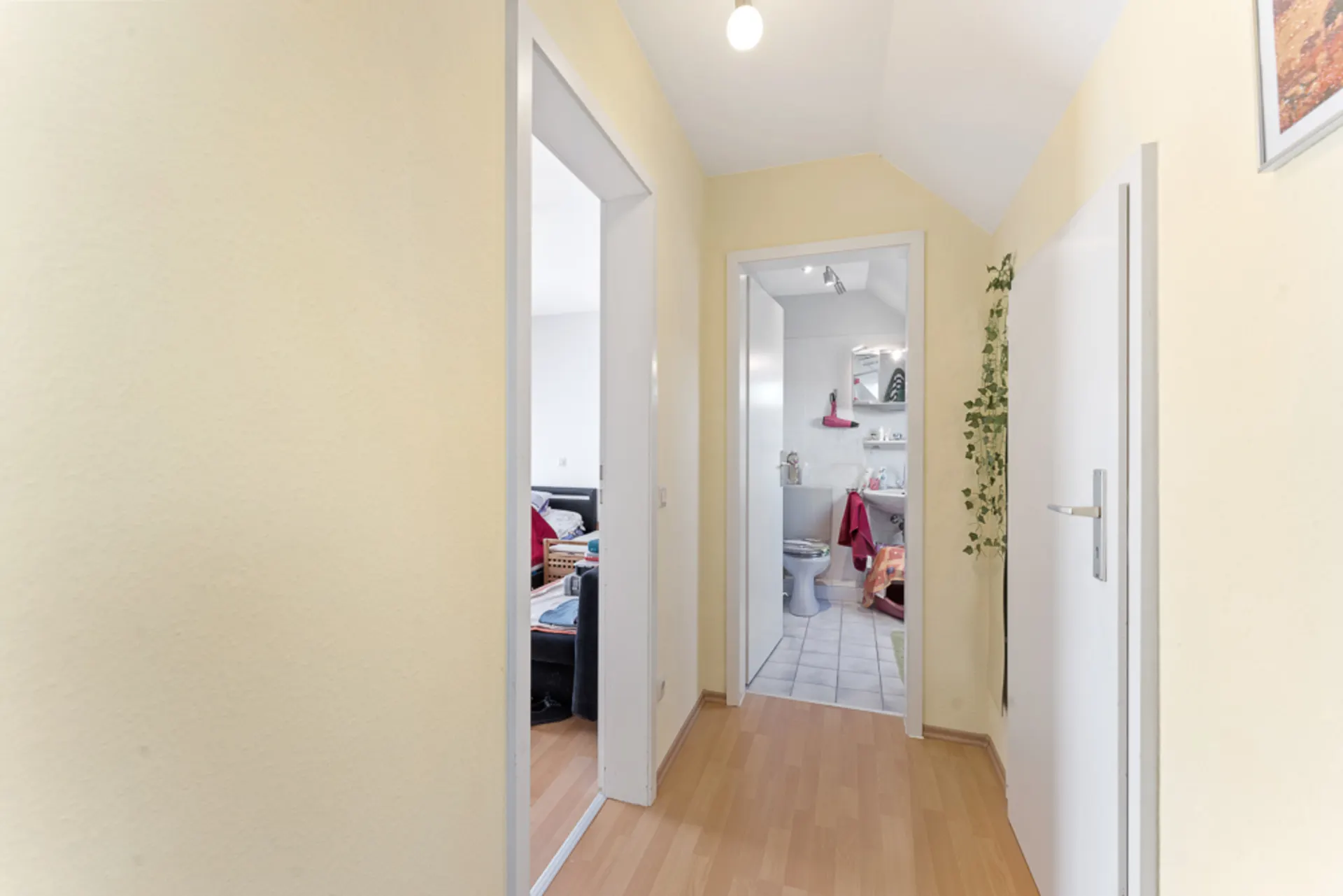 Heller Flur mit Türen zu einem Wohnzimmer und einem Badezimmer, Holzboden und gelben Wänden.