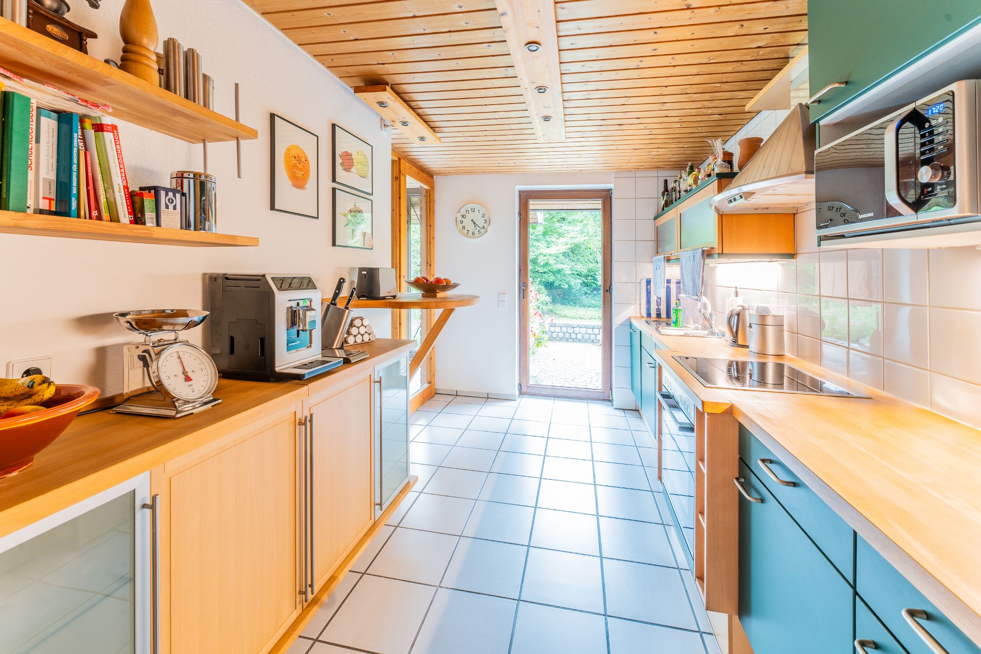Helle, moderne Küche mit Holzdecke, offenen Regalen, Geräten und Zugang zum Garten.