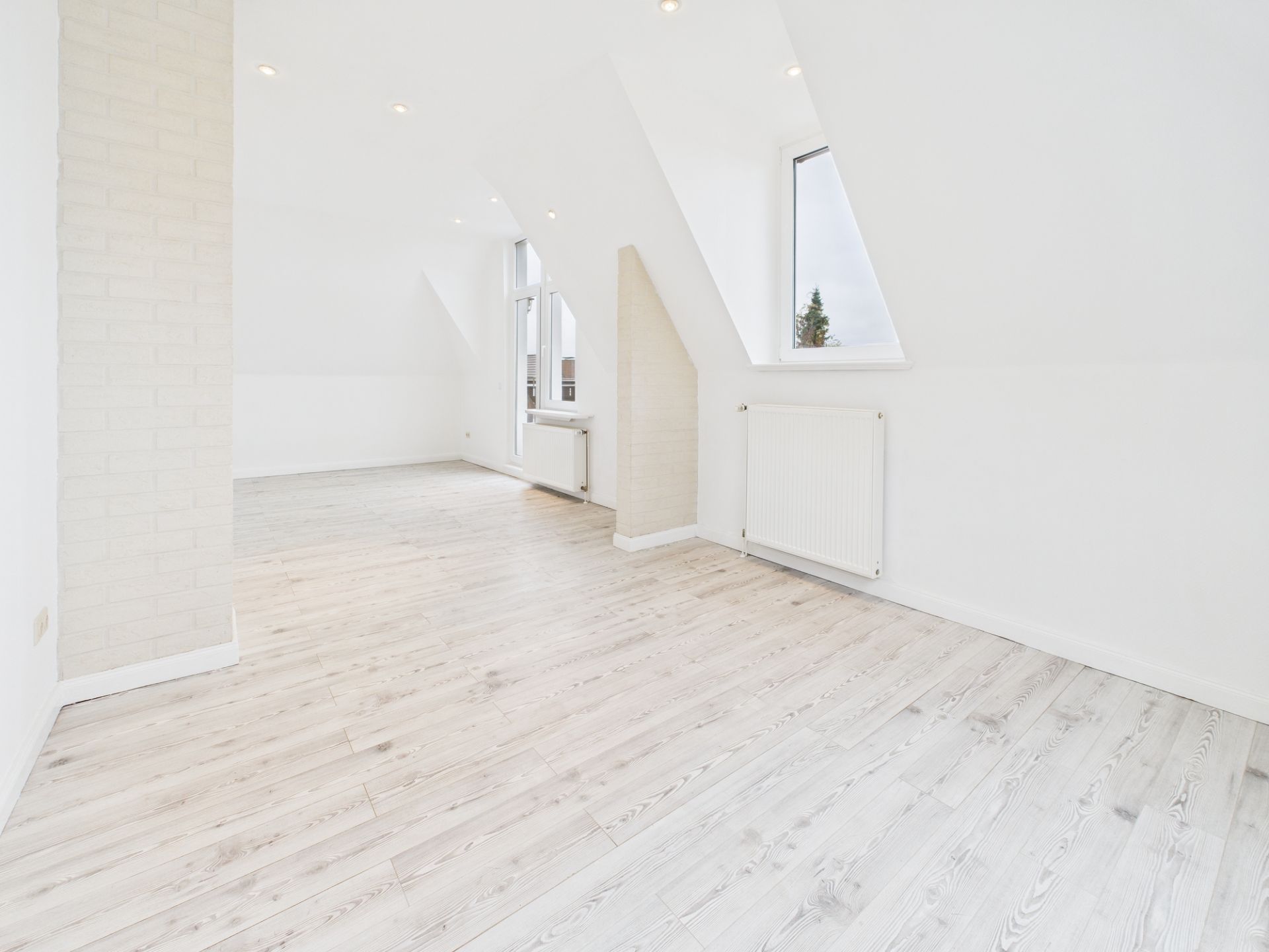 Heller Raum mit schrägen Decken, großen Fenstern und hellem Holzfußboden.