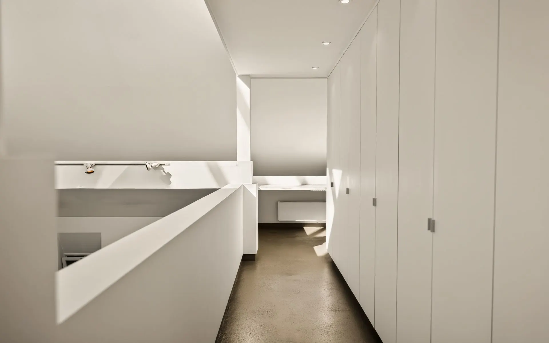 Heller Flur mit weißen Wandschränken und Betonboden in einem Wohnhaus.