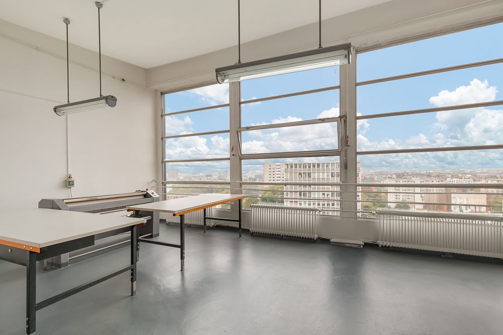 Heller Raum mit großen Fenstern, zwei Tischen und Blick auf die Stadt.
