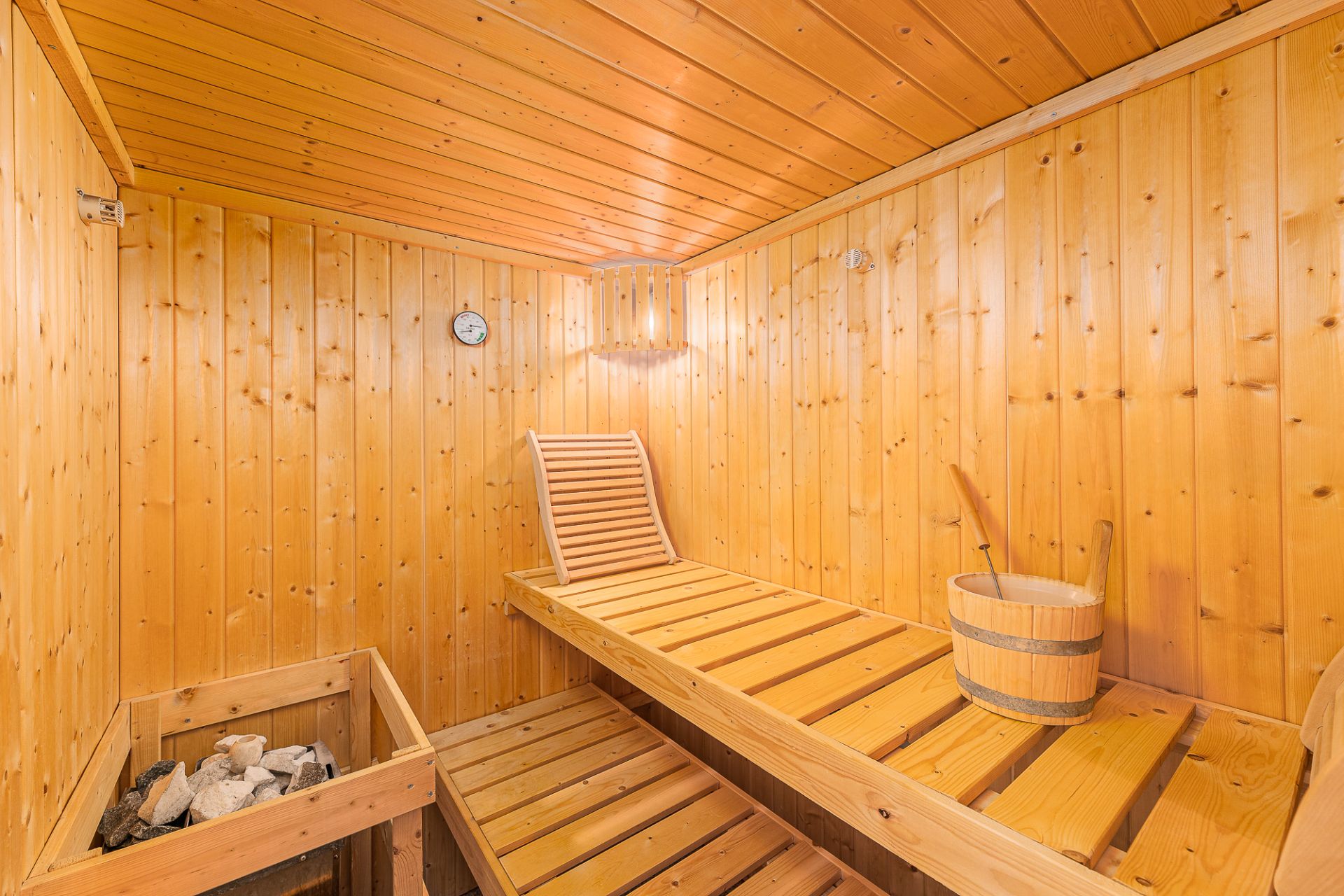 Holzsauna mit Bank, Saunaeimer, Saunaofen und Wanduhr in einem Wohnhaus.