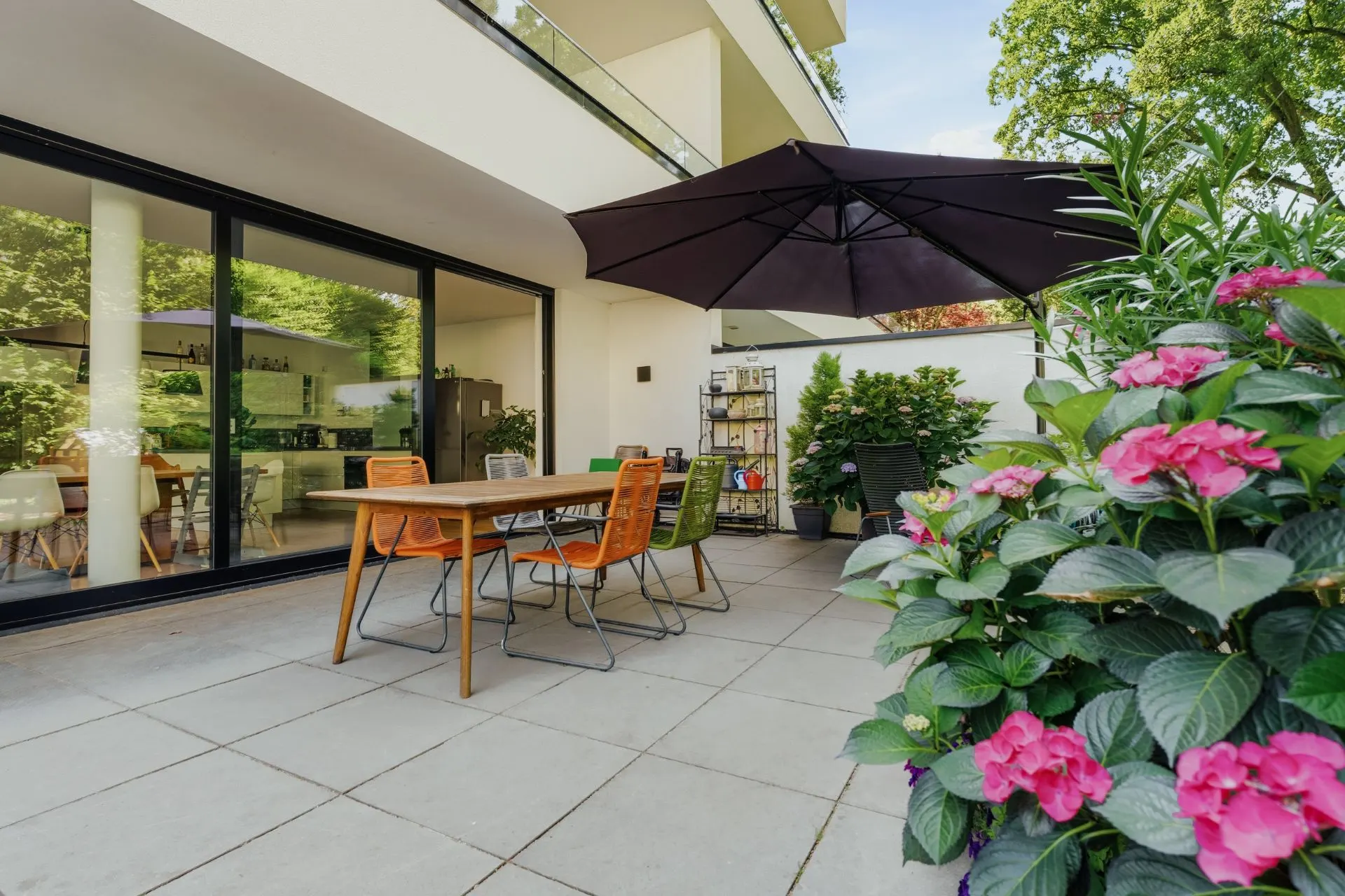 Moderne Terrasse mit Holztisch, Stühlen, großem Sonnenschirm und Blumen im Vordergrund.