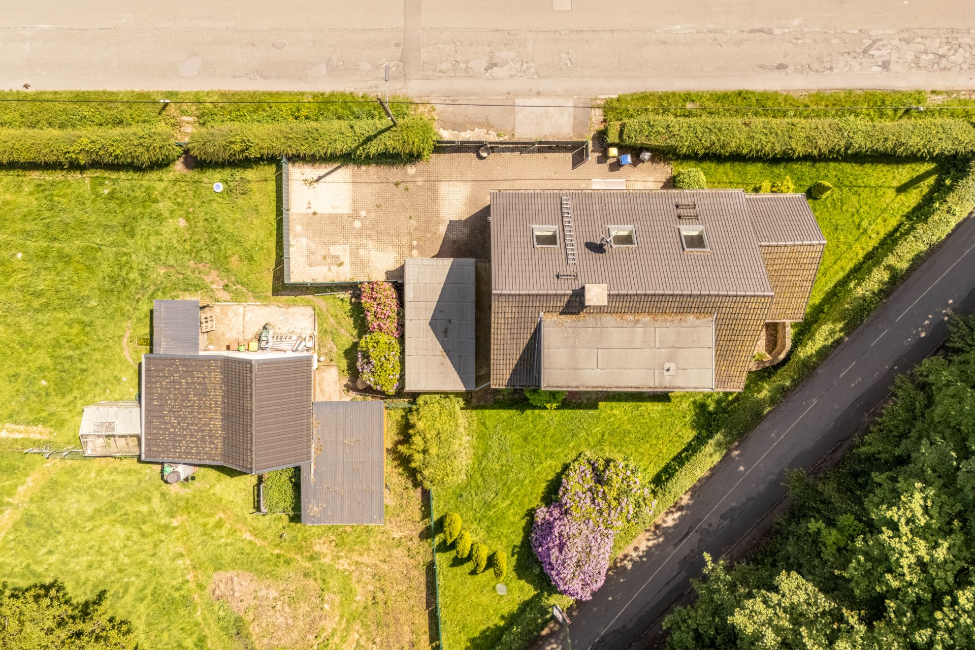 Luftaufnahme eines Wohnhauses mit Nebengebäude, Garten und angrenzender Straße.