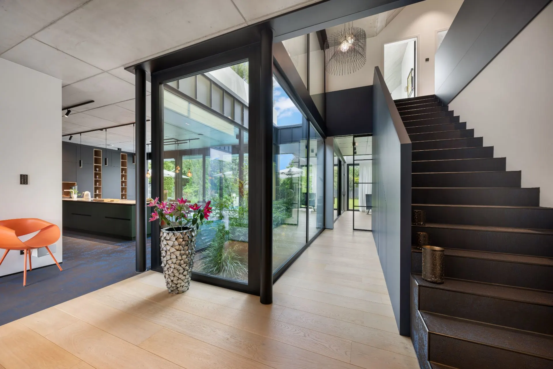 Moderner Flur mit Holzfußboden, Glaswänden, Treppe und Blick in den Garten.