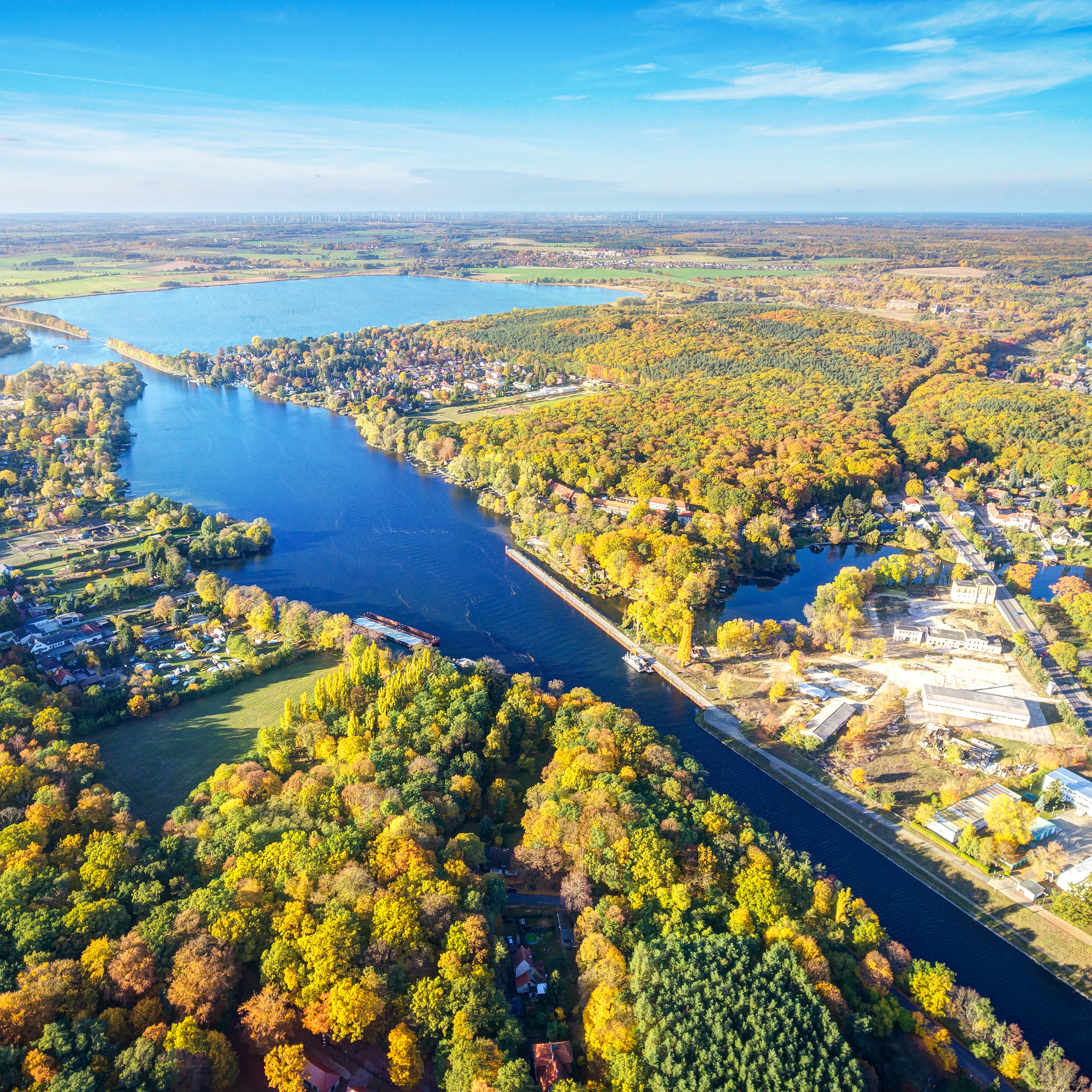 Luftaufnahme eines Flusses mit Boot, umgeben von Wald und Häusern bei Sonnenlicht.