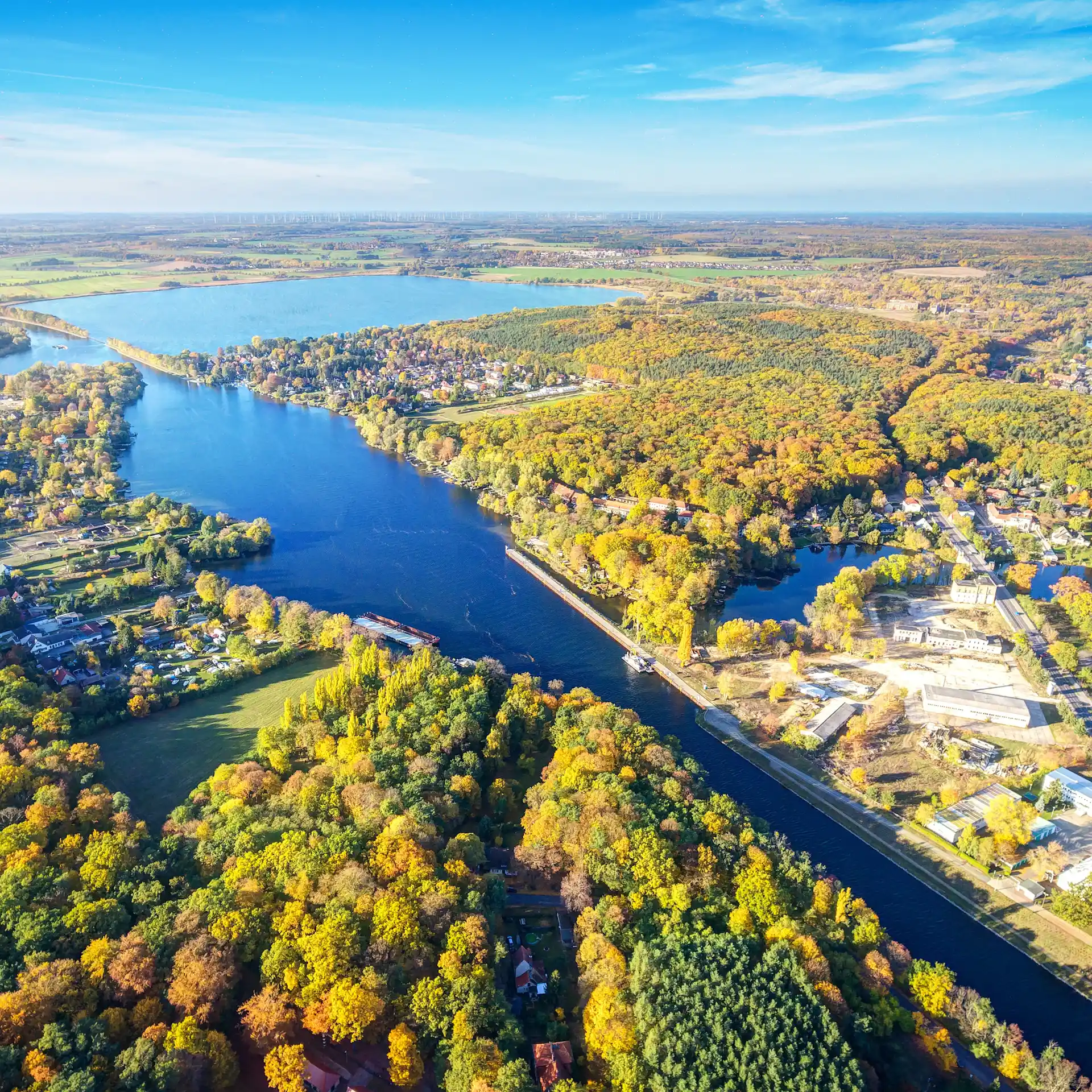 Luftaufnahme eines Flusses mit Boot, umgeben von Wald und Häusern bei Sonnenlicht.