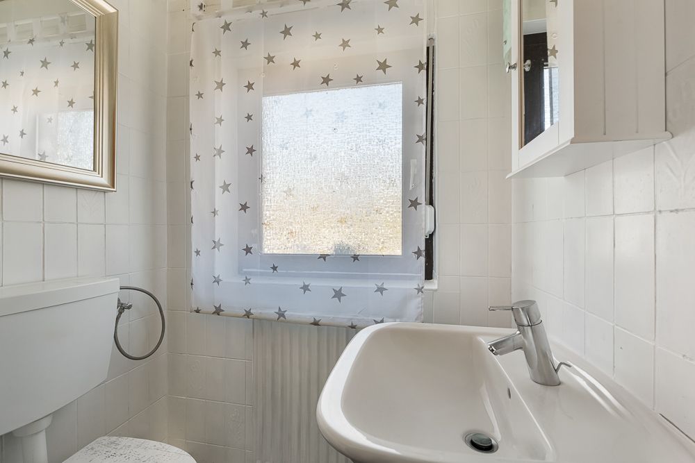 Kleines Bad mit weißem Waschbecken, WC und Fenster mit Vorhang mit Sternenmuster.