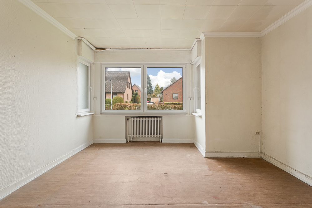 Leerer Raum mit großem Fenster, Blick auf Nachbarhäuser, unter dem Fenster steht ein Heizkörper.
