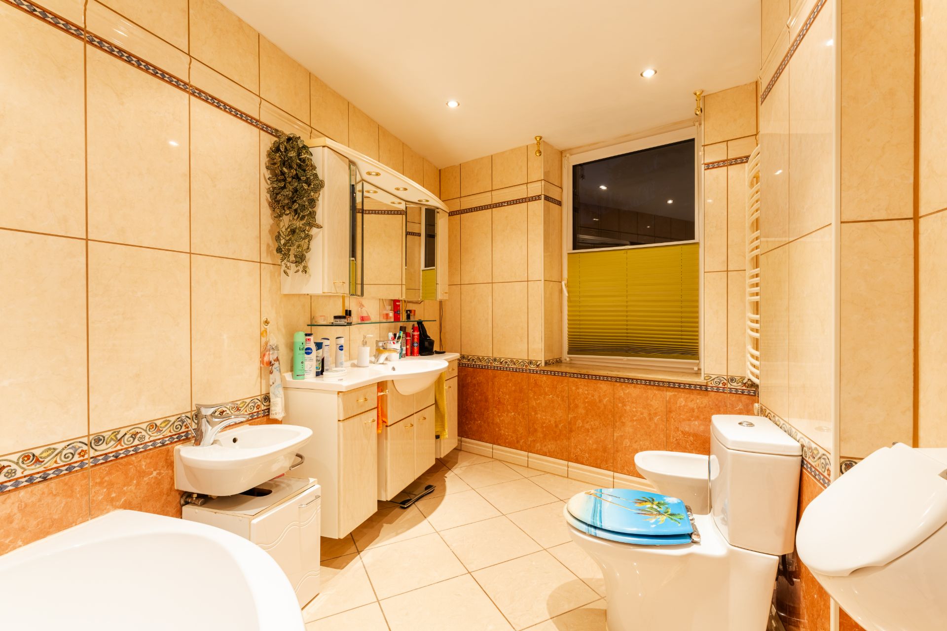 Modernes Badezimmer mit großem Spiegel, Waschbecken, Toilette und Badewanne mit hellen Fliesen.