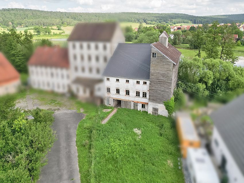 Altes, mehrstöckiges Haus mit grauem Dach und großem, bewachsenem Vorgarten.