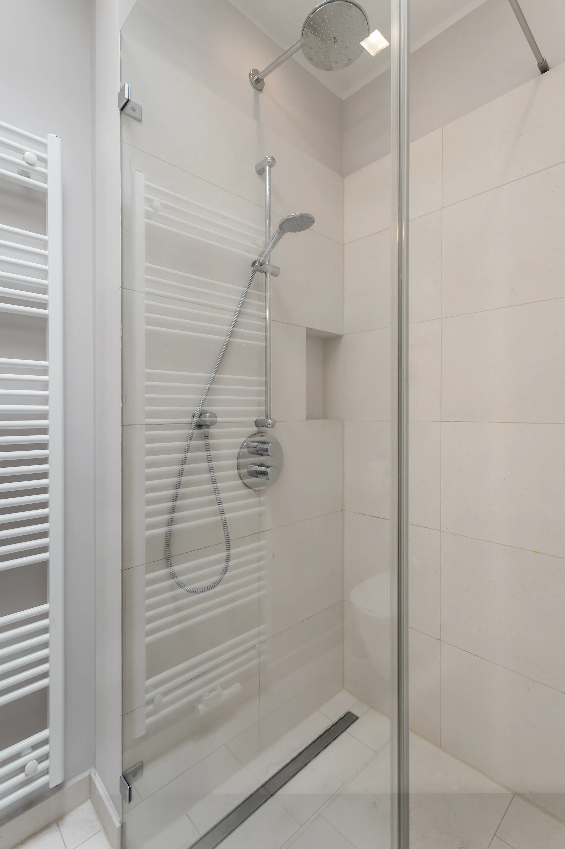 Moderne Dusche mit Glaswand, Handtuchheizkörper und hellem Fliesenboden.