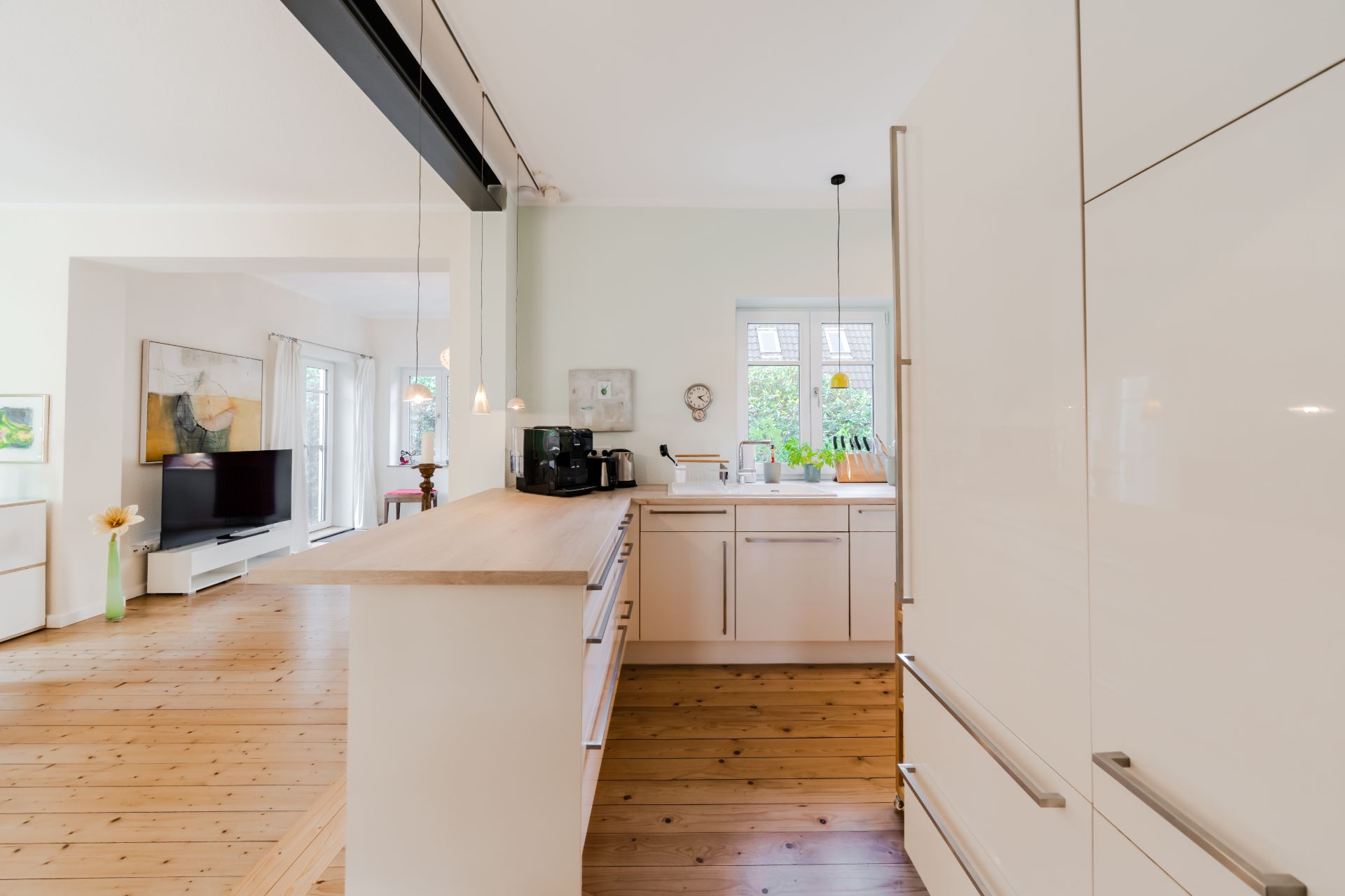 Helle offene Küche mit Holzboden, weißen Schränken und Blick ins Wohnzimmer.