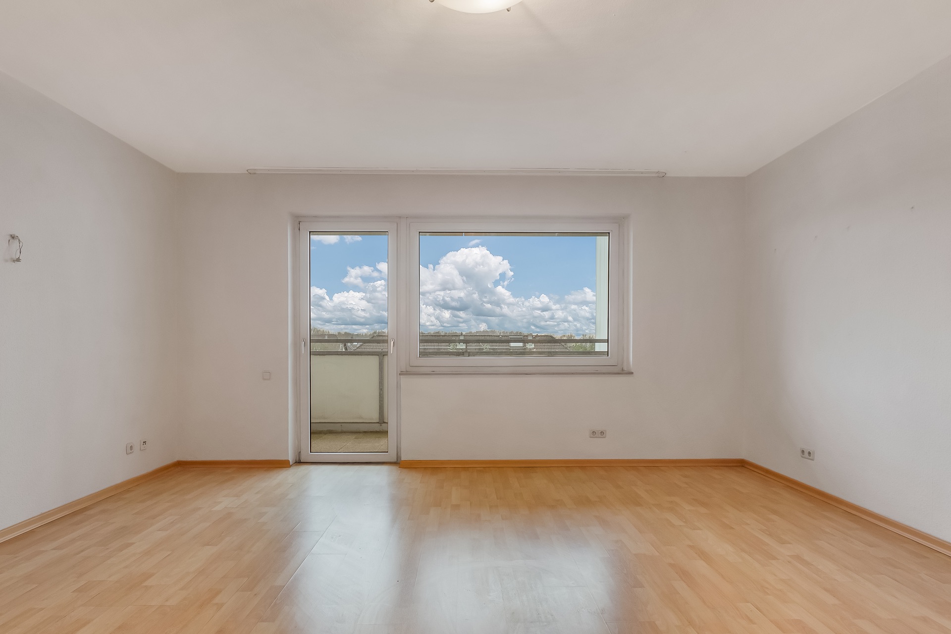 Leerer Raum mit Holzfußboden und großem Fenster, das auf einen Balkon führt.