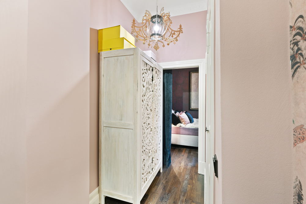 Flur mit hellem Schrank, gelben Boxen und Blick in ein Schlafzimmer mit Bett.